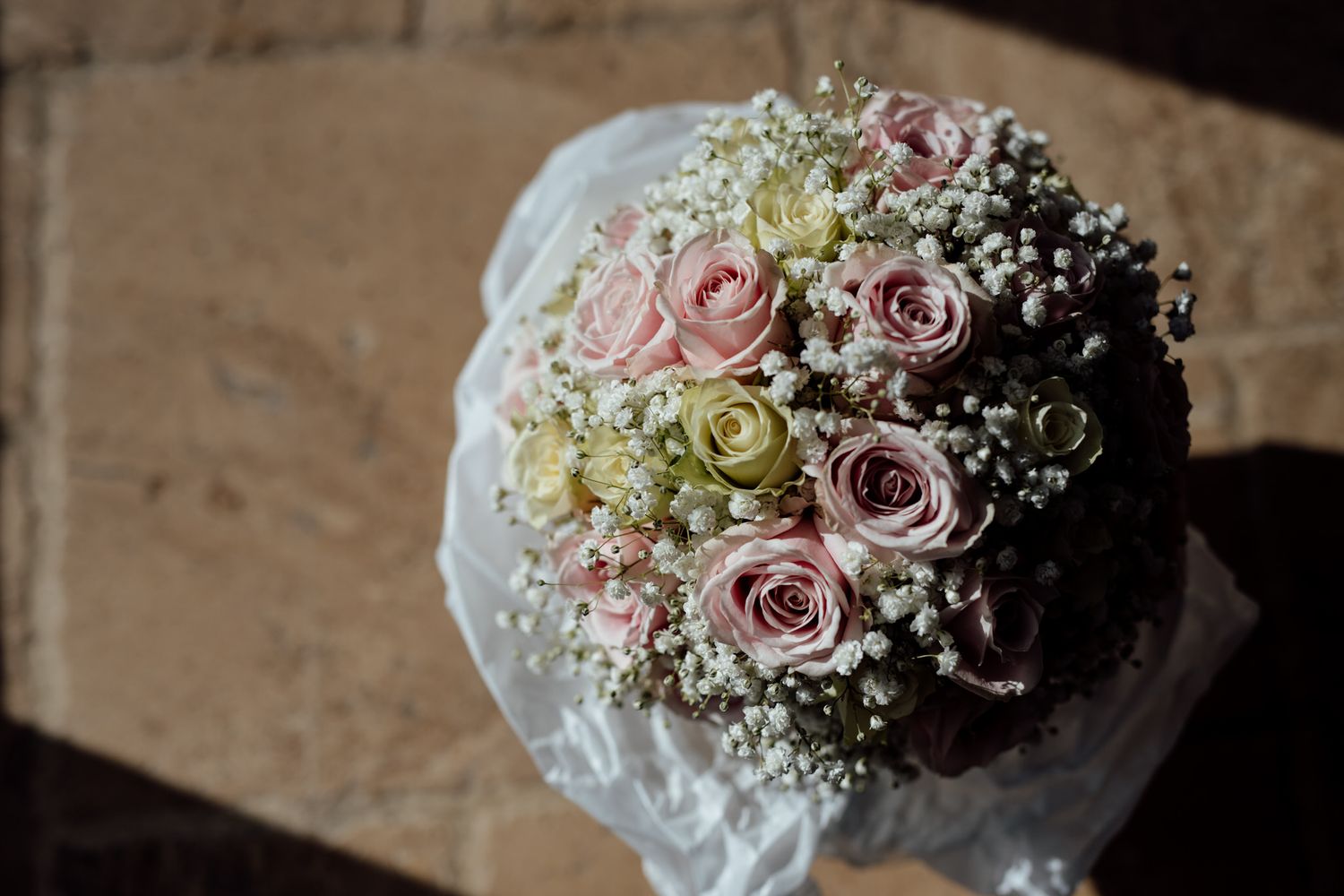 Wedding bouquet featuring pink roses and baby's breath against rustic wooden background.