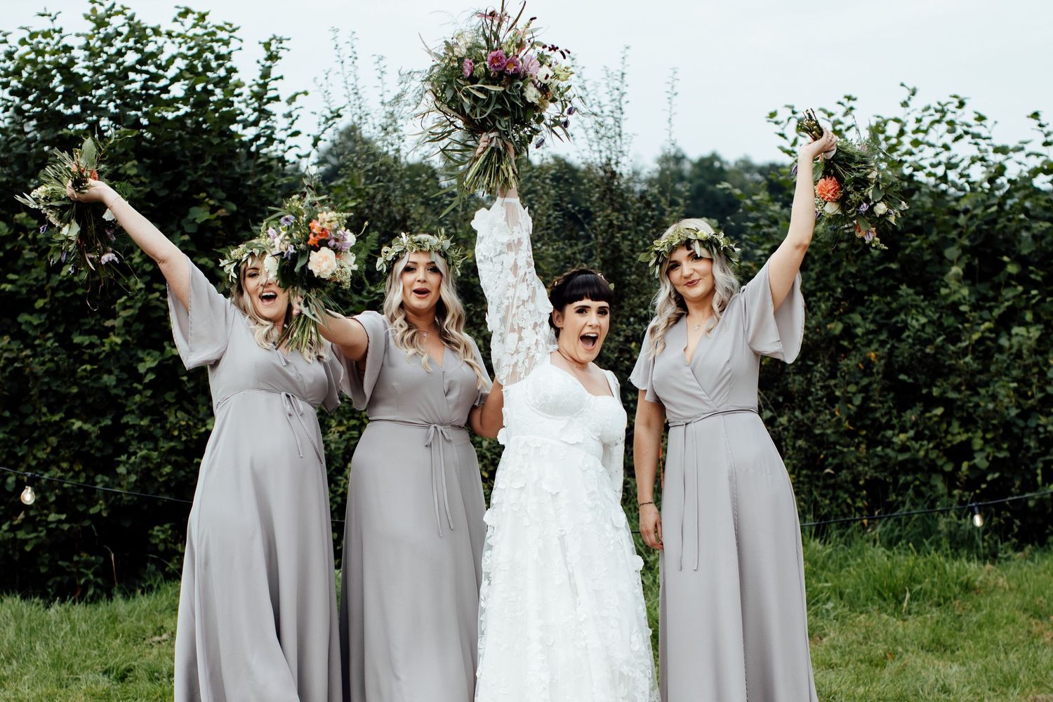 Bridal party in gray dresses celebrating outdoors against a natural green backdrop.
