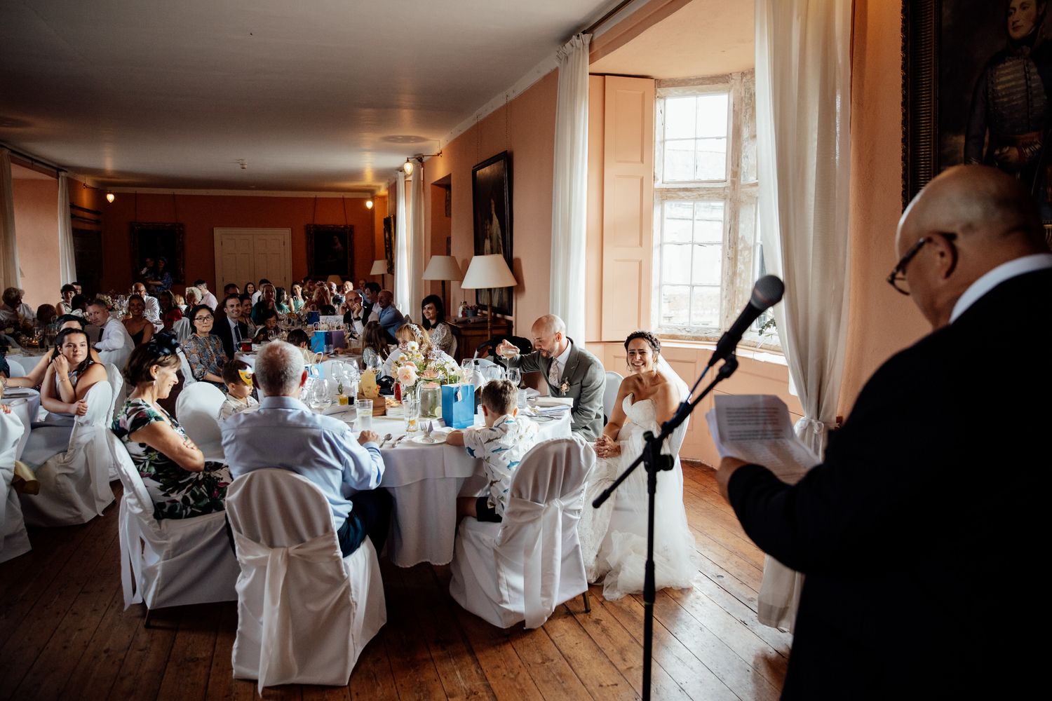 Wedding reception in a grand hall with guests seated at decorated tables.
