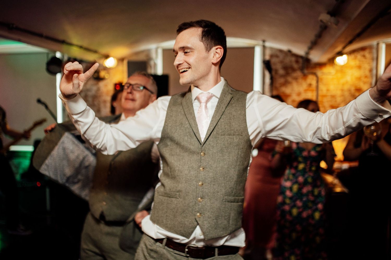 Wedding reception celebration with guests dancing in a dimly lit venue.