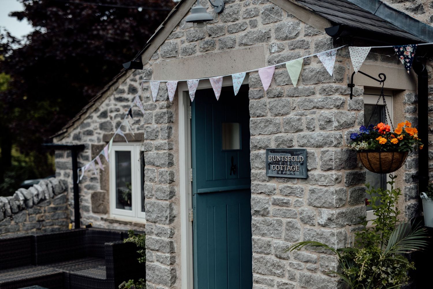 Stone cottage exterior with teal doors and hanging flower baskets creates rustic wedding venue atmosphere.