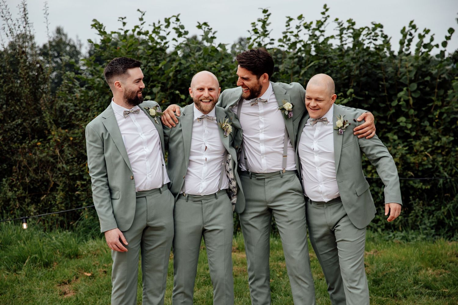 Wedding party in matching light gray suits pose together outdoors.