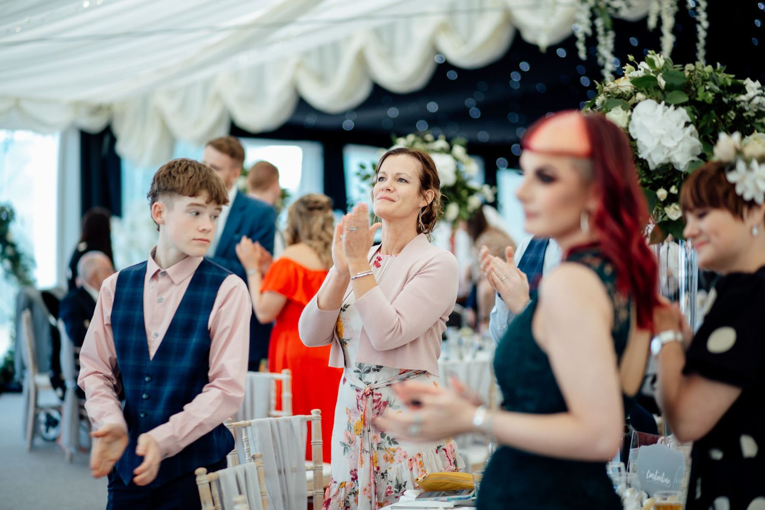 Wedding reception guests mingling under white draped ceiling decorations.