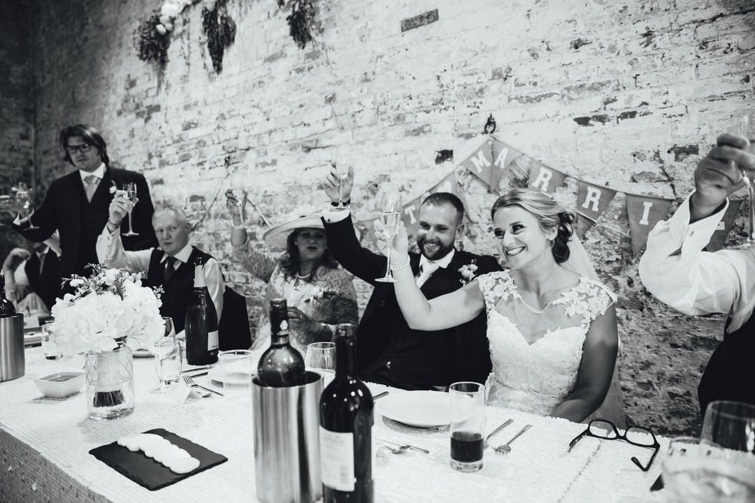 A black and white reception photo showing newlyweds at their wedding dinner table.