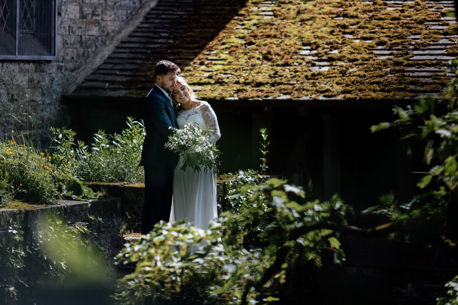 A couple in wedding attire poses for romantic photos in a garden setting with natural greenery.