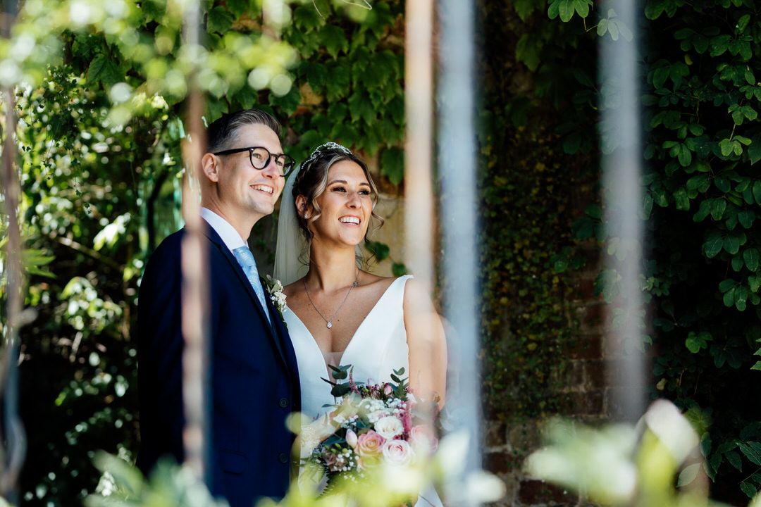 Romantic garden wedding portrait among white pillars and greenery.