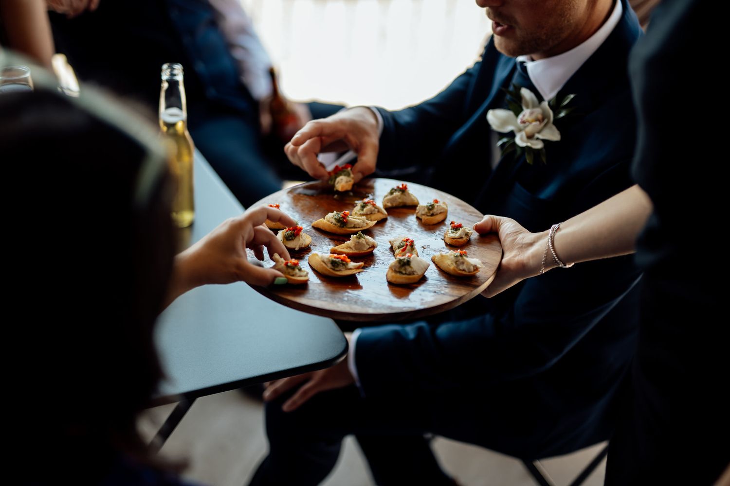Guests reaching for appetizers being served on a white plate at an elegant event.