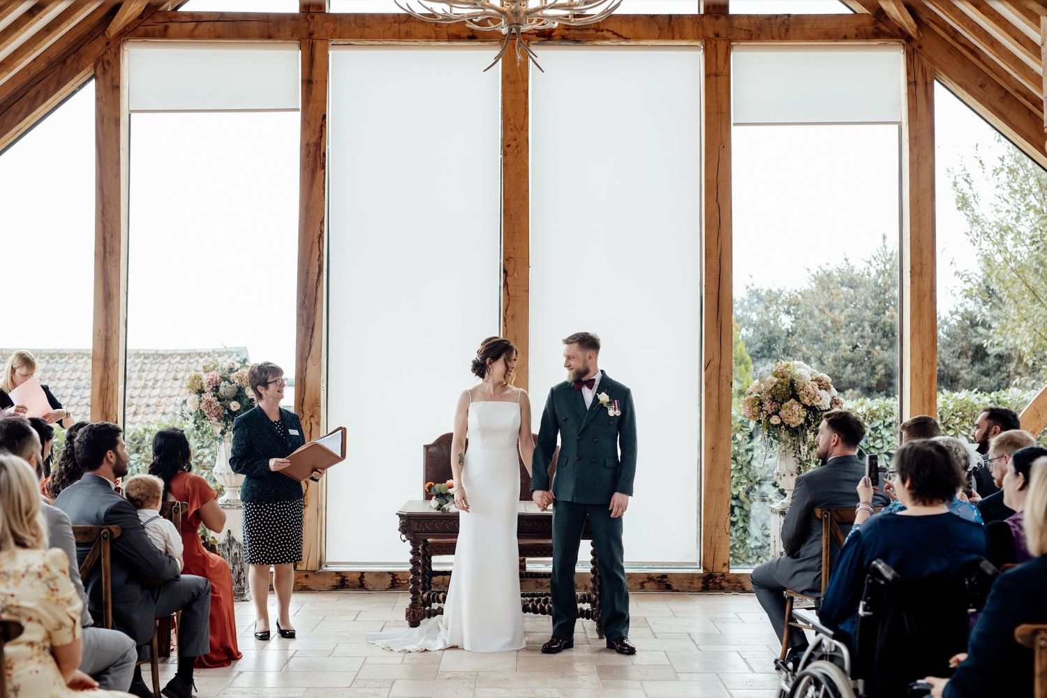 Wedding ceremony in a modern venue with large windows and wooden beams.