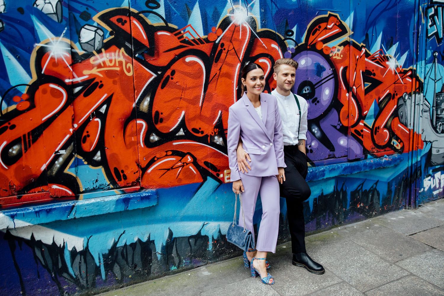 A couple poses against a vibrant blue and red graffiti wall mural.