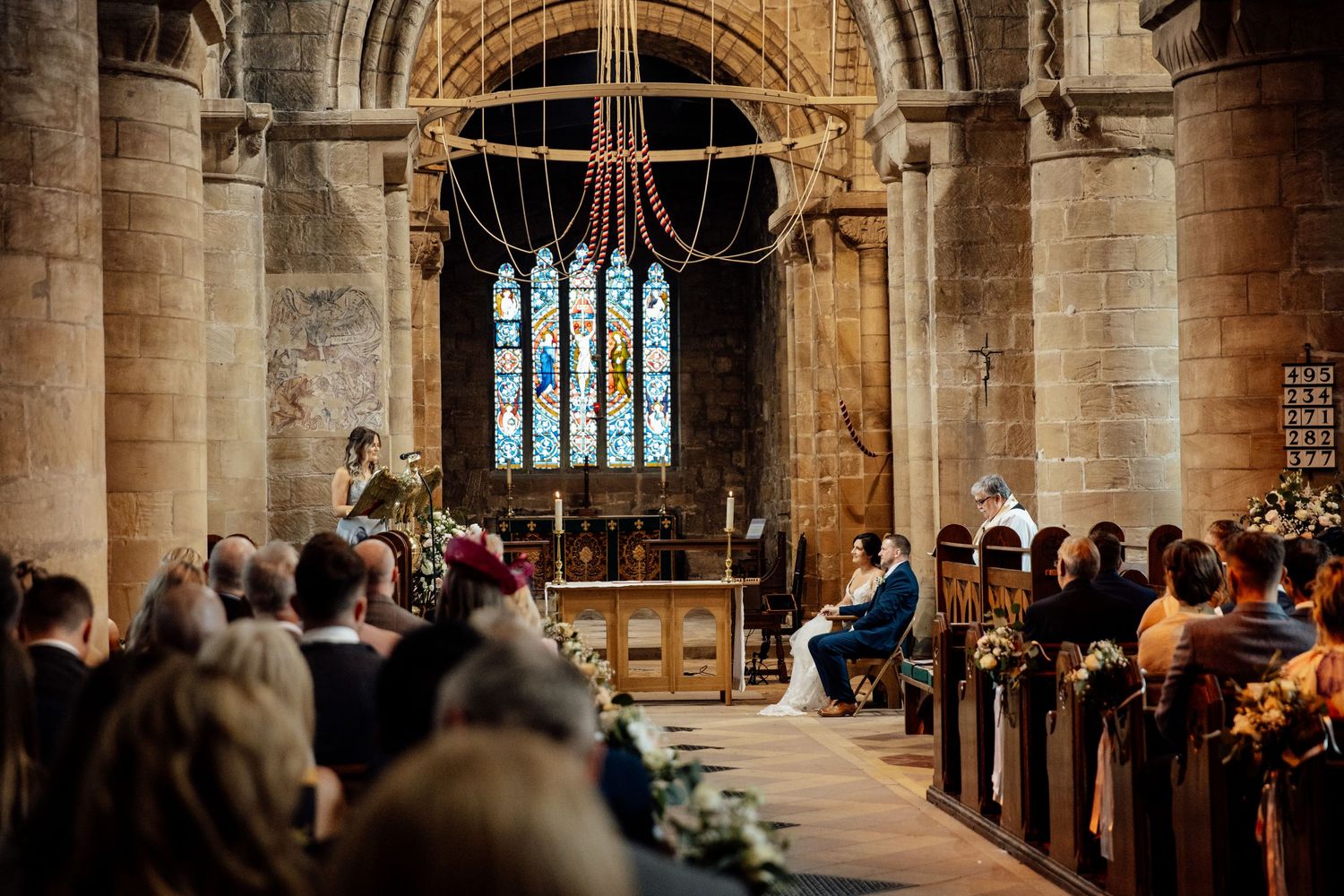 Interior of historic stone church with vaulted ceilings and stained glass windows during ceremony.
