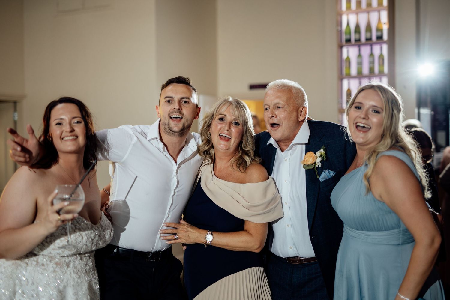 Wedding party members celebrate joyfully during reception festivities in an indoor venue.