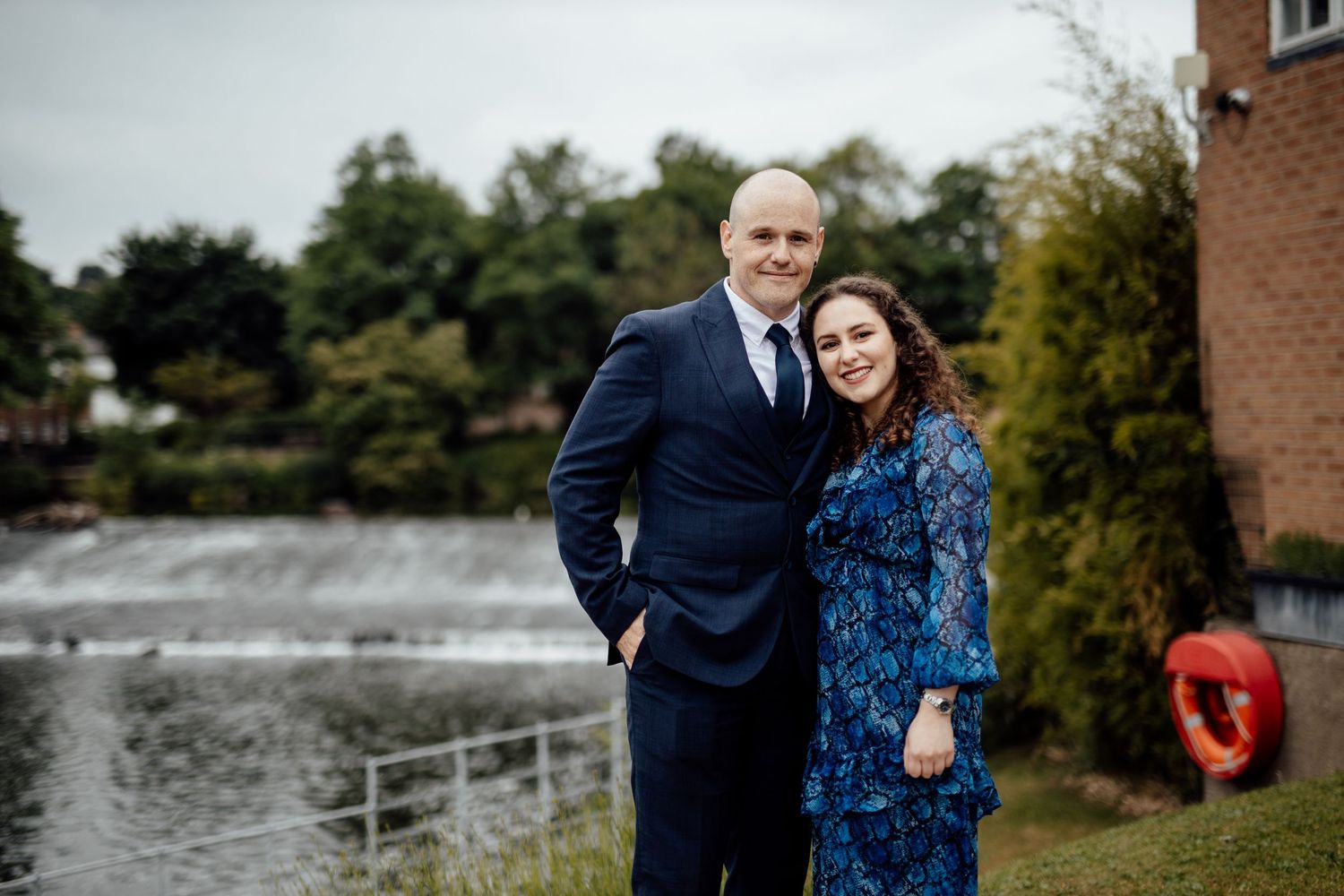 A couple poses for romantic portraits near a lakeside setting.