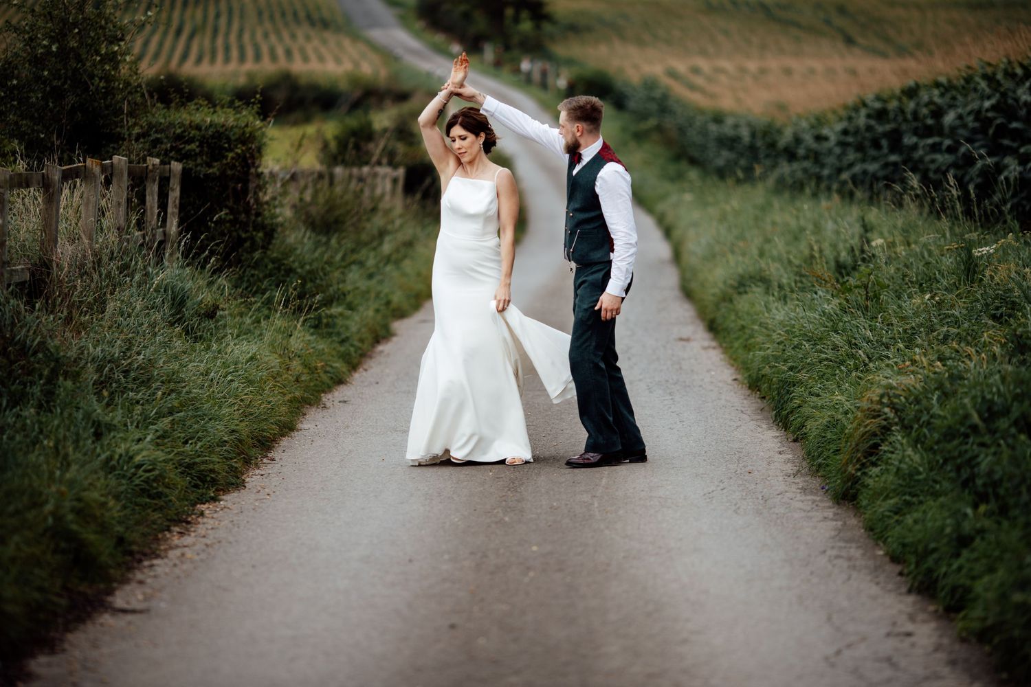 Wedding couple walks along a countryside path surrounded by lush greenery.