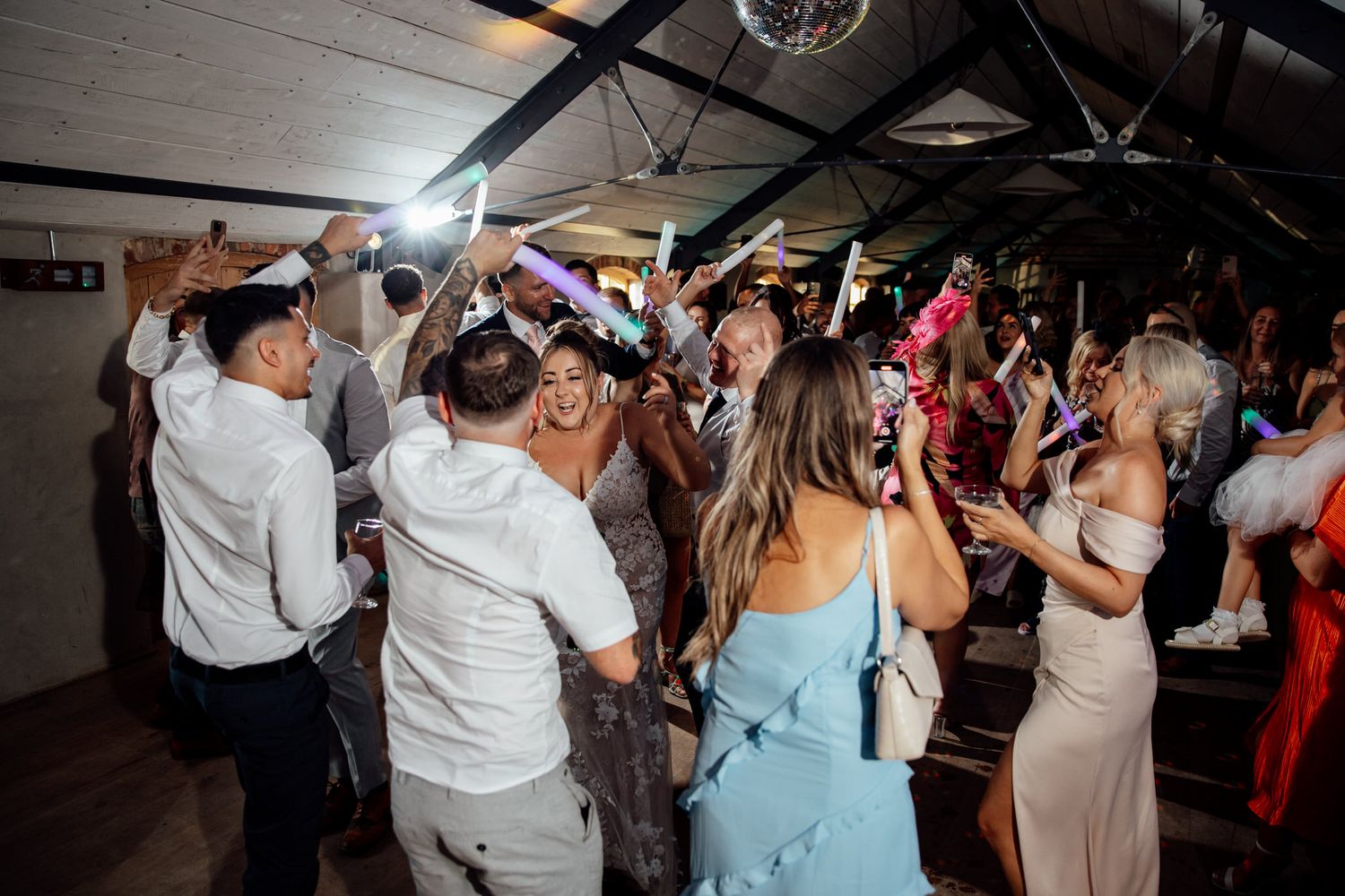 Energetic wedding reception dance floor filled with celebrating guests under dim lighting.