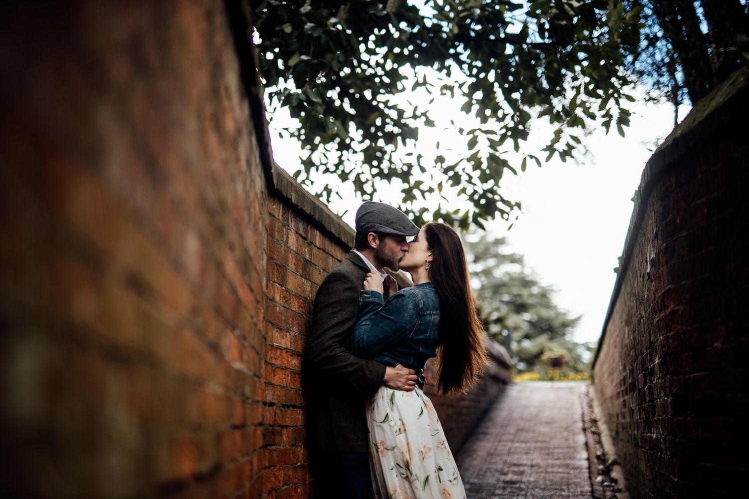 A couple walks through a brick archway surrounded by greenery.
