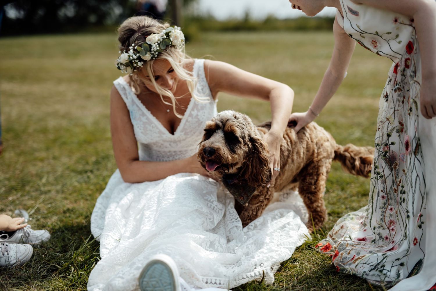 Wedding party playfully posing in a grassy outdoor setting with white dresses and floral bouquets.