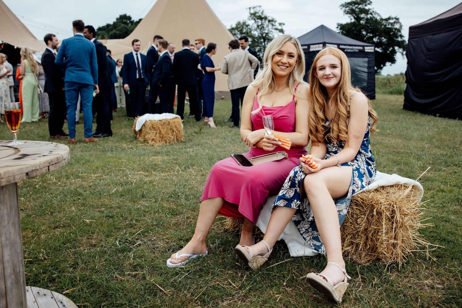 Wedding guests relaxing on hay bales at an outdoor reception.