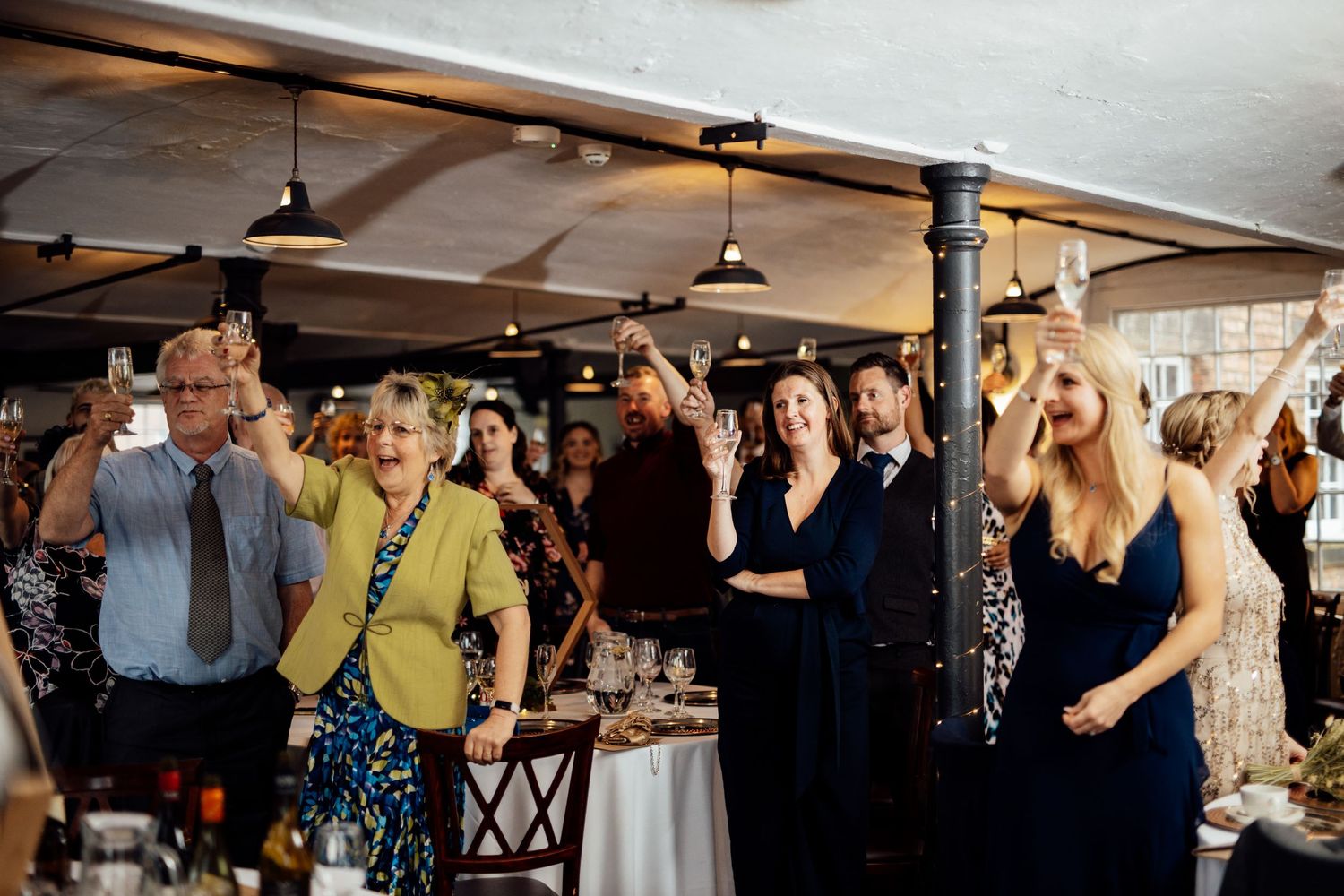 Wedding guests celebrating and raising their hands during a reception in an industrial venue.