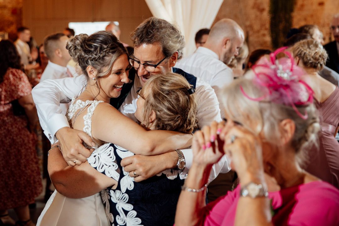 Wedding guests embrace while dancing at a reception in a rustic brick venue.