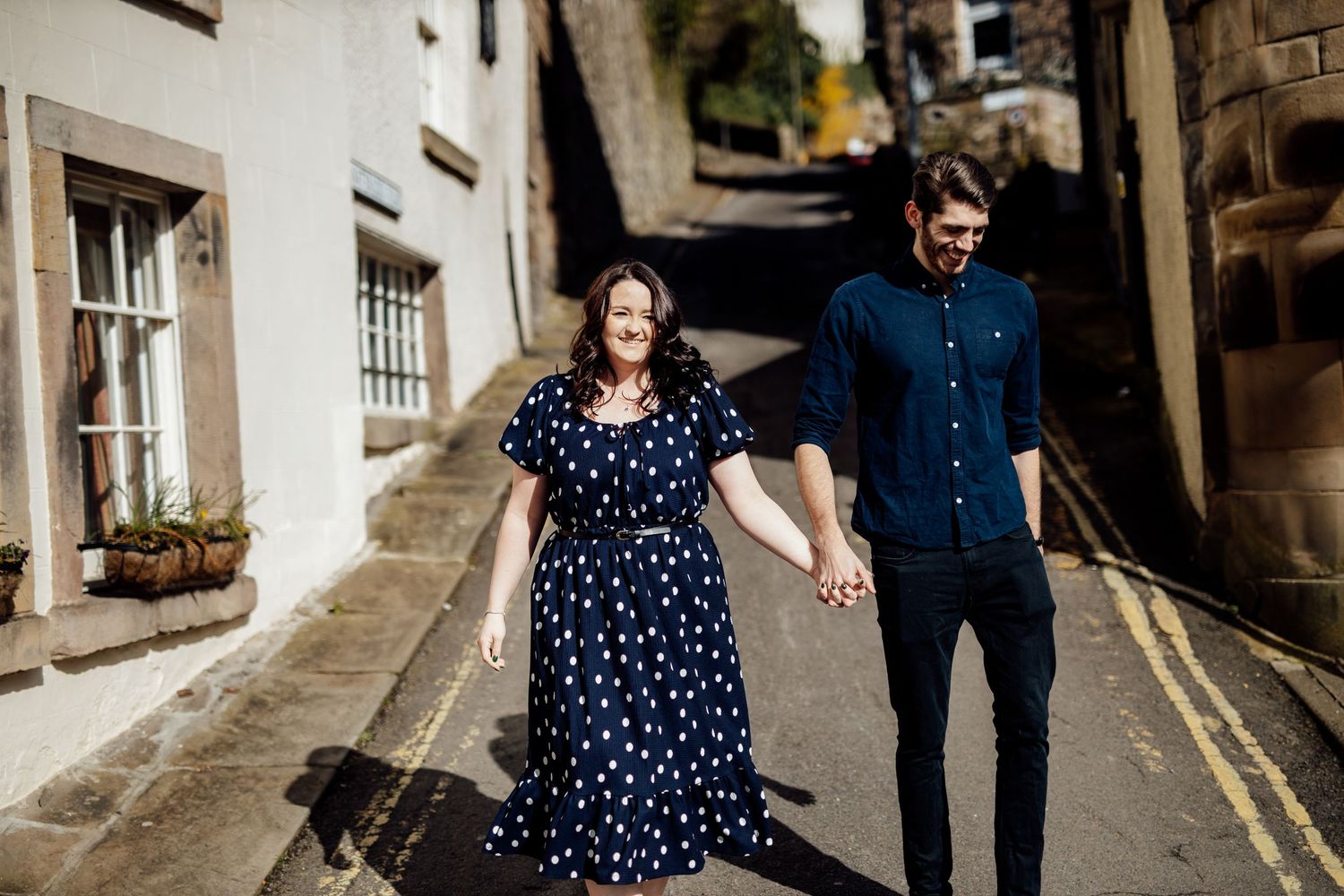 A couple walks hand in hand up a narrow European-style street with white buildings.