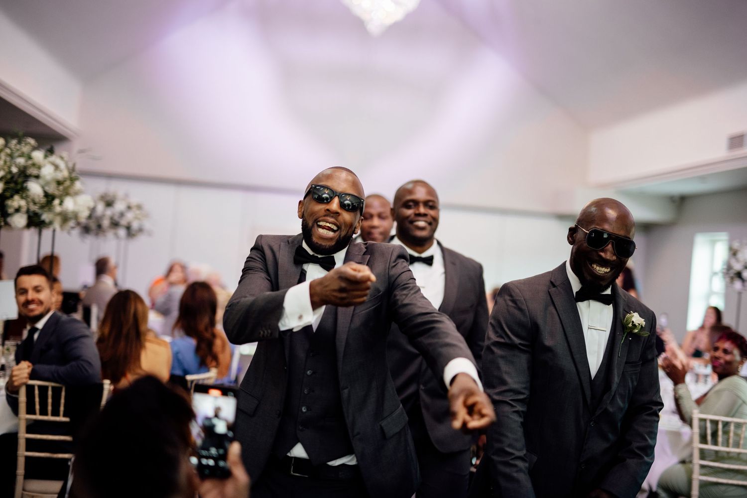 Wedding party members in formal black attire gather at reception venue.