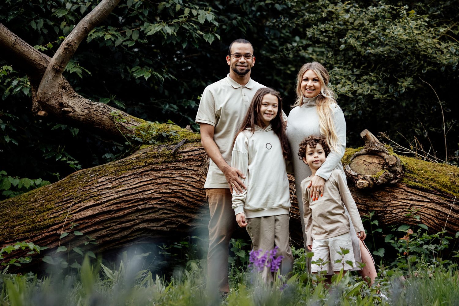 A family explores a wooded area with fallen trees during a casual outdoor photo session.