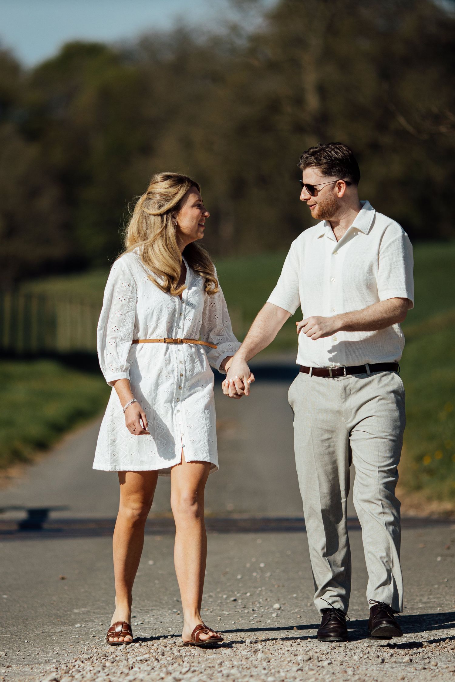 Two people in casual white and beige outfits stroll along a gravel path.
