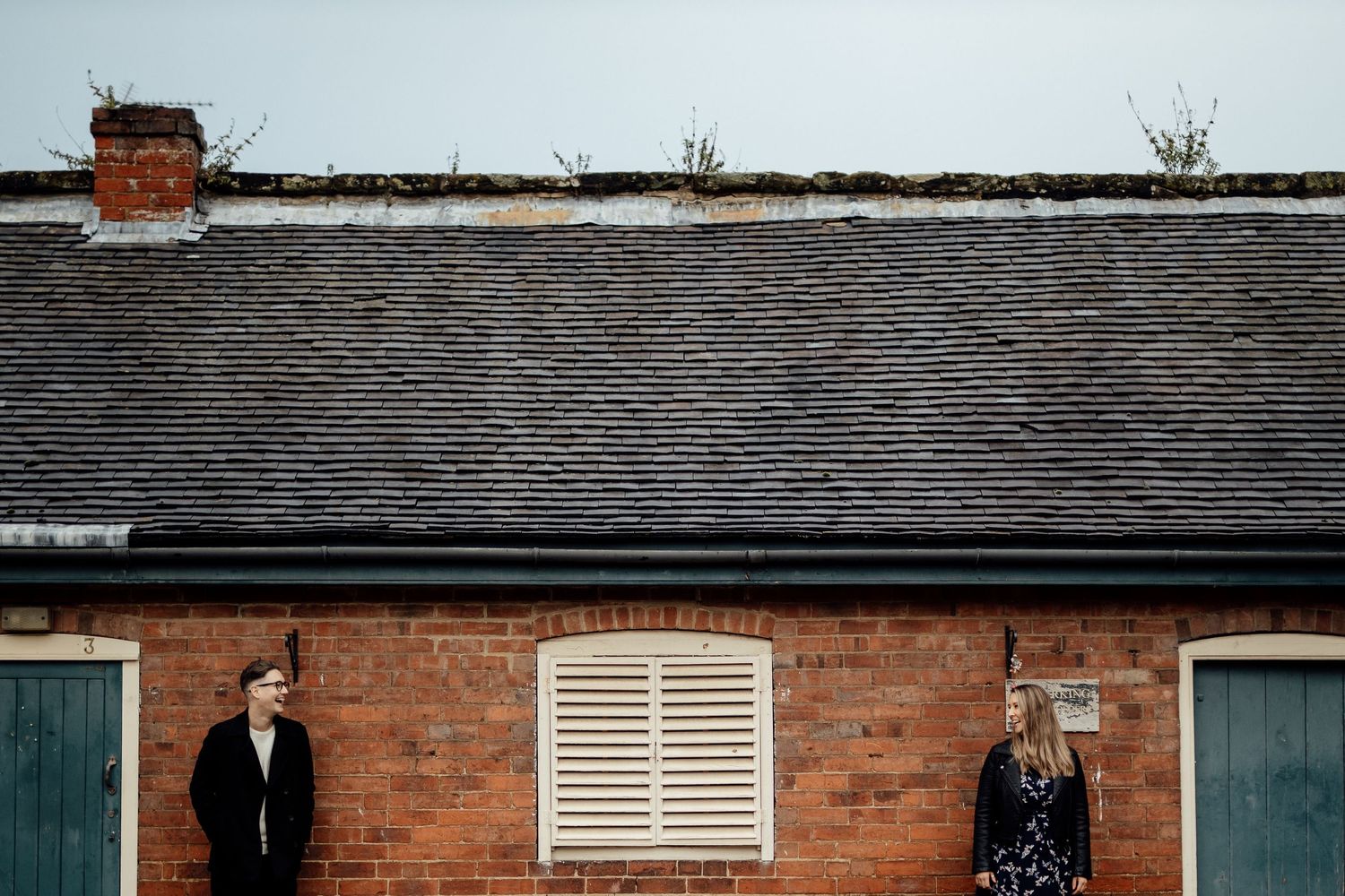 Couple poses against brick building with white architectural details.