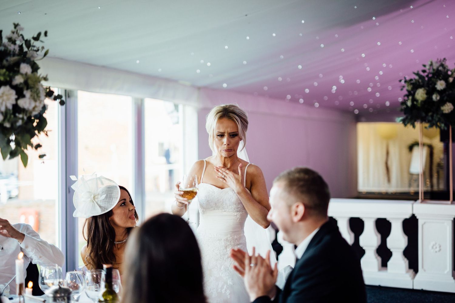 Wedding guests raise their glasses in a toast during an indoor reception celebration.