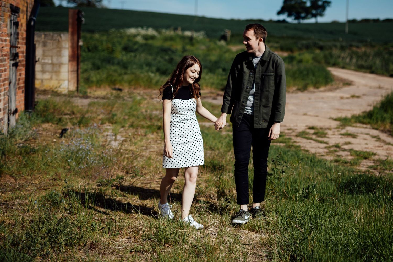 A couple walking together on a grassy path surrounded by green countryside.