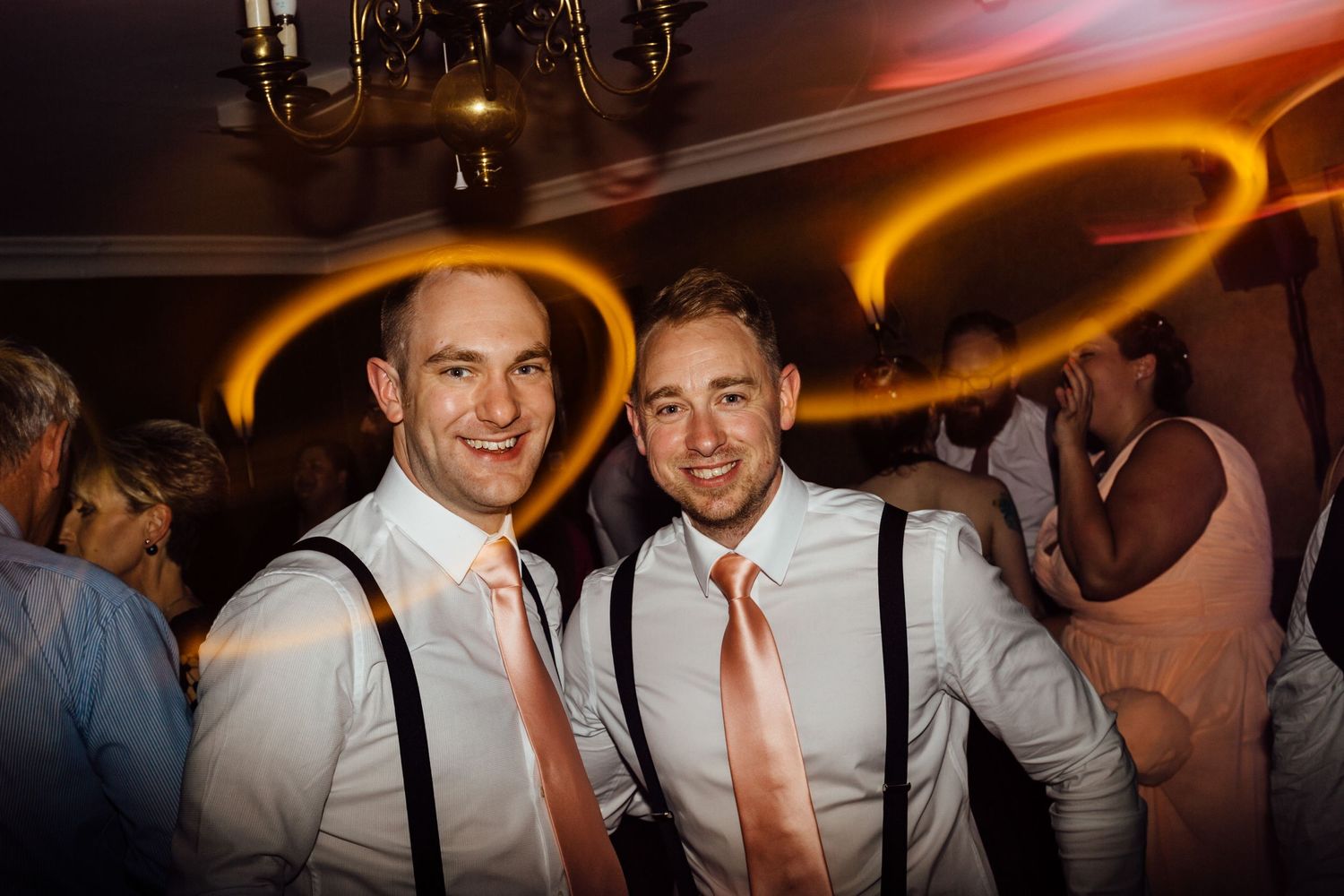 Wedding guests dance and celebrate on a dimly lit dance floor with colorful lighting effects.