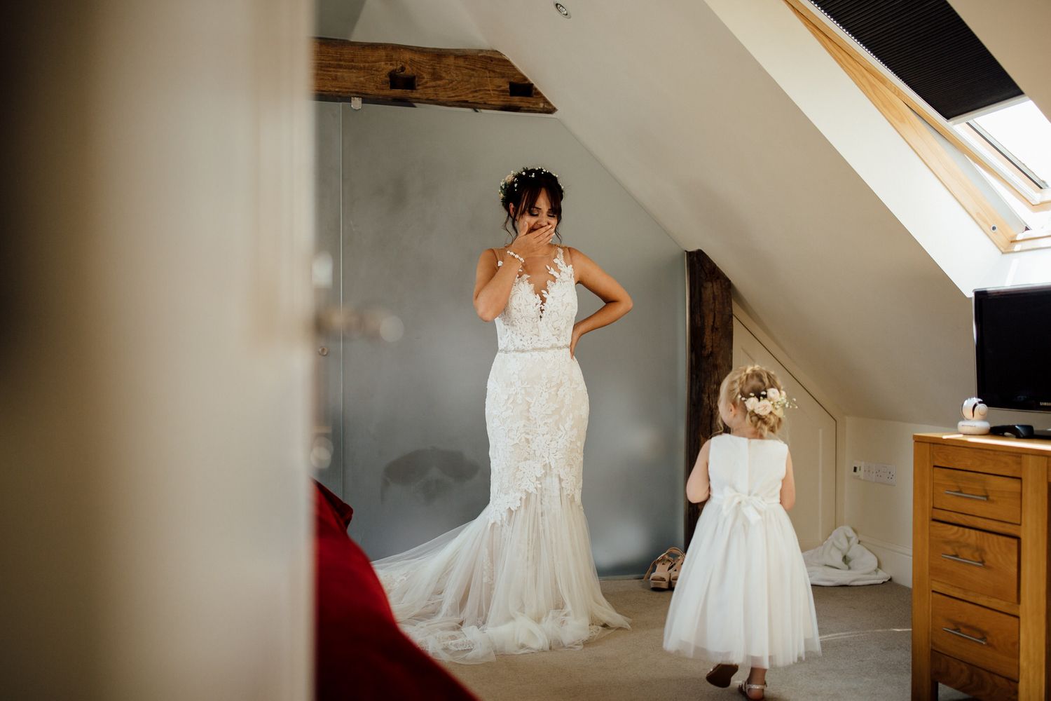 White wedding dress hanging in a sunlit room with rustic wooden beams.
