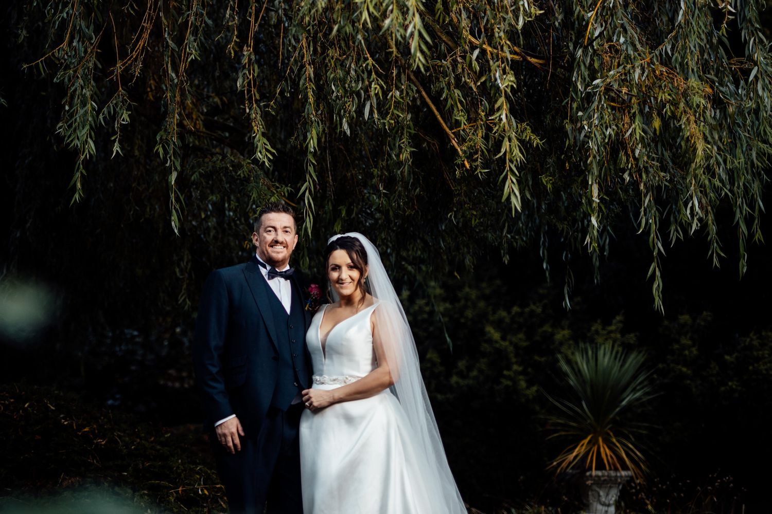 Elegant wedding portraits captured under drooping willow trees at sunset.