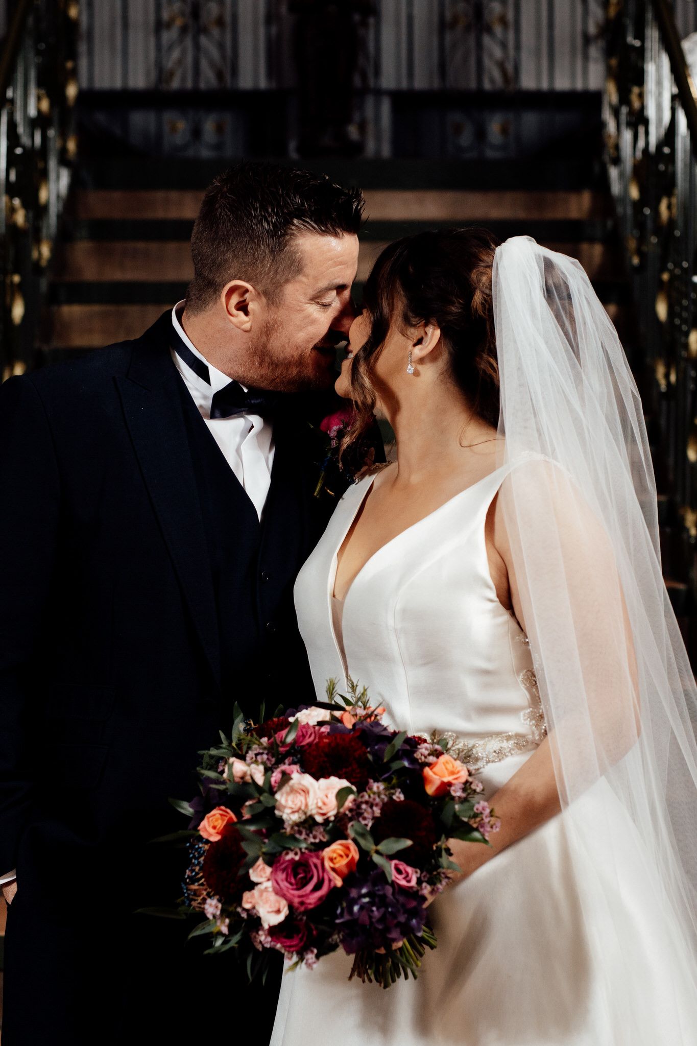 Intimate wedding couple portraits with dramatic lighting and burgundy floral bouquet.