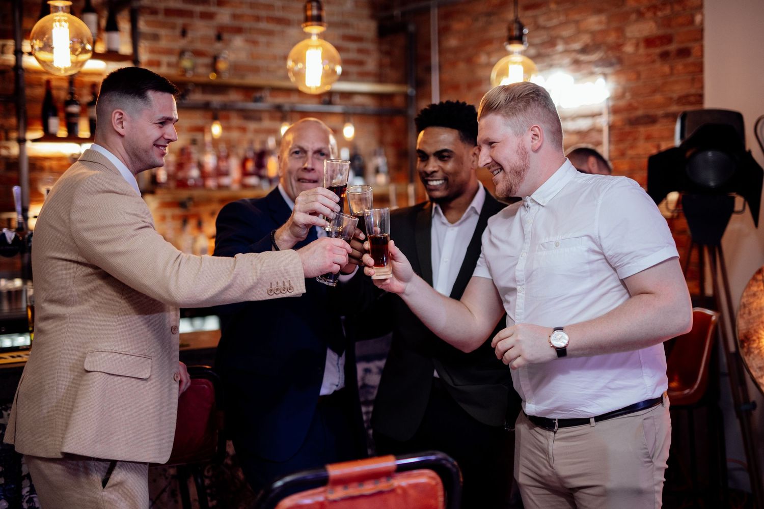 Guests celebrating and toasting at a brick-walled venue with warm lighting.