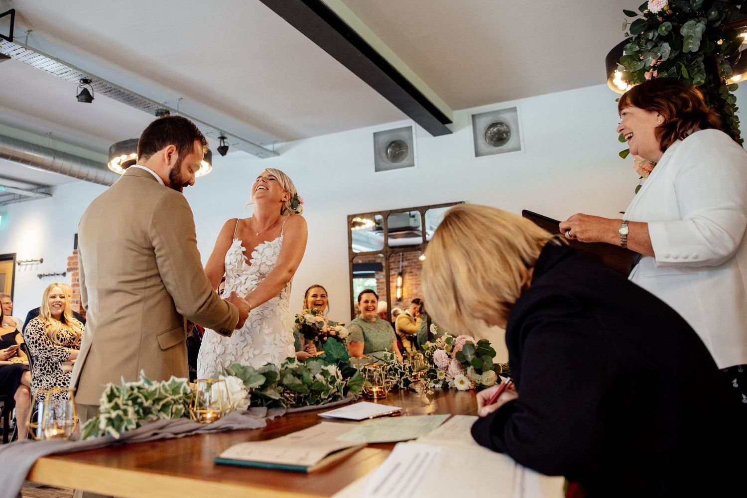 Wedding guests gathered around tables at an intimate indoor reception venue.