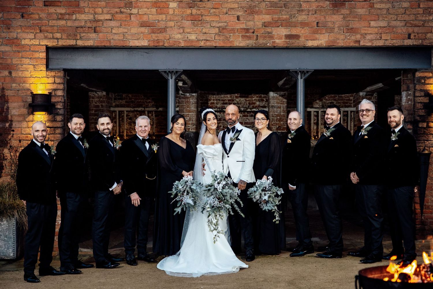 Large wedding party lines up for formal photo against industrial brick backdrop.