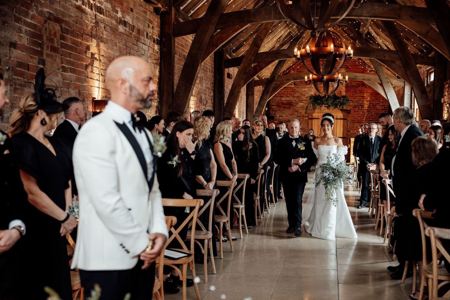 Wedding ceremony in a grand rustic venue with exposed wooden beams and brick walls.