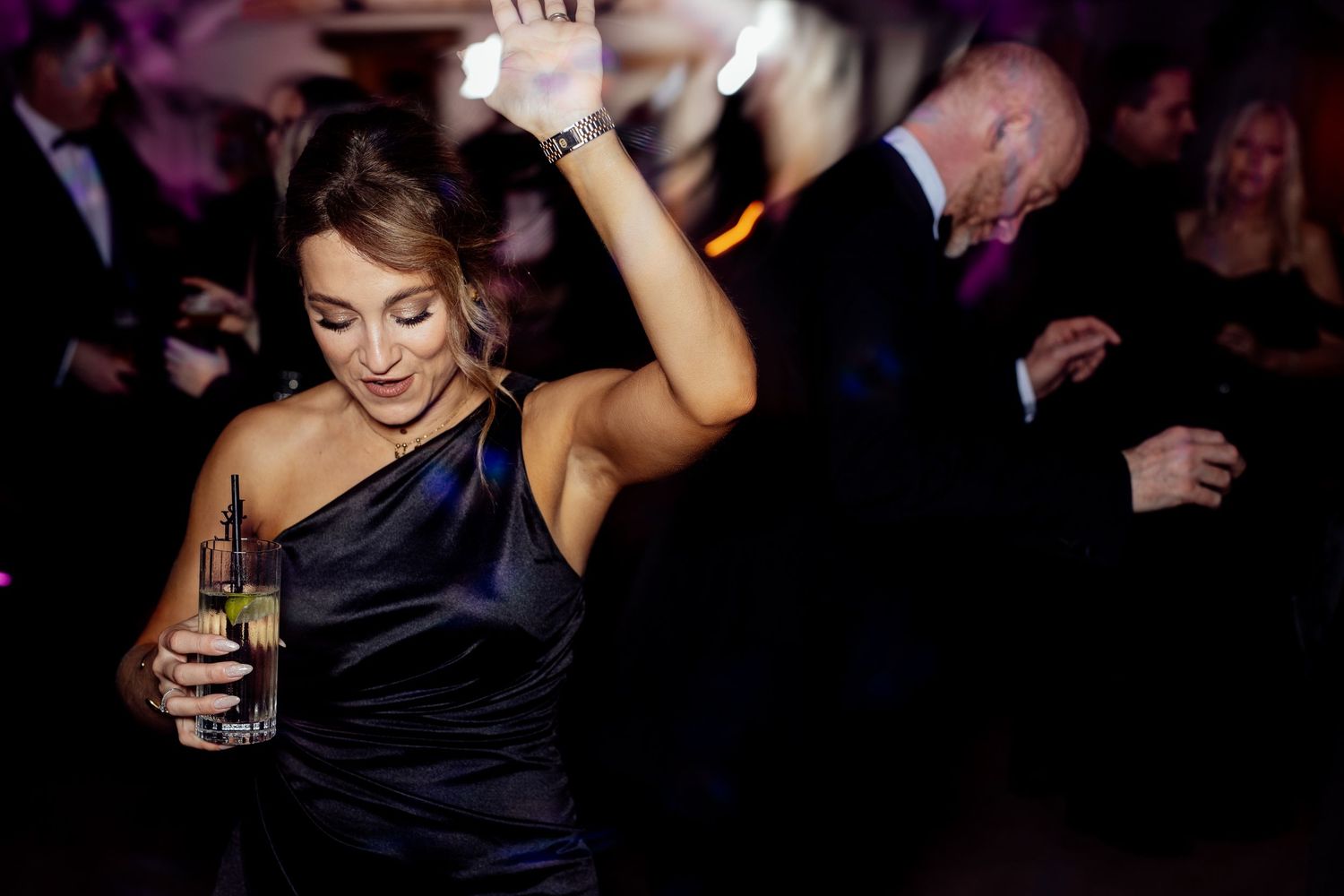 Wedding reception dance party with purple mood lighting and guests dancing.
