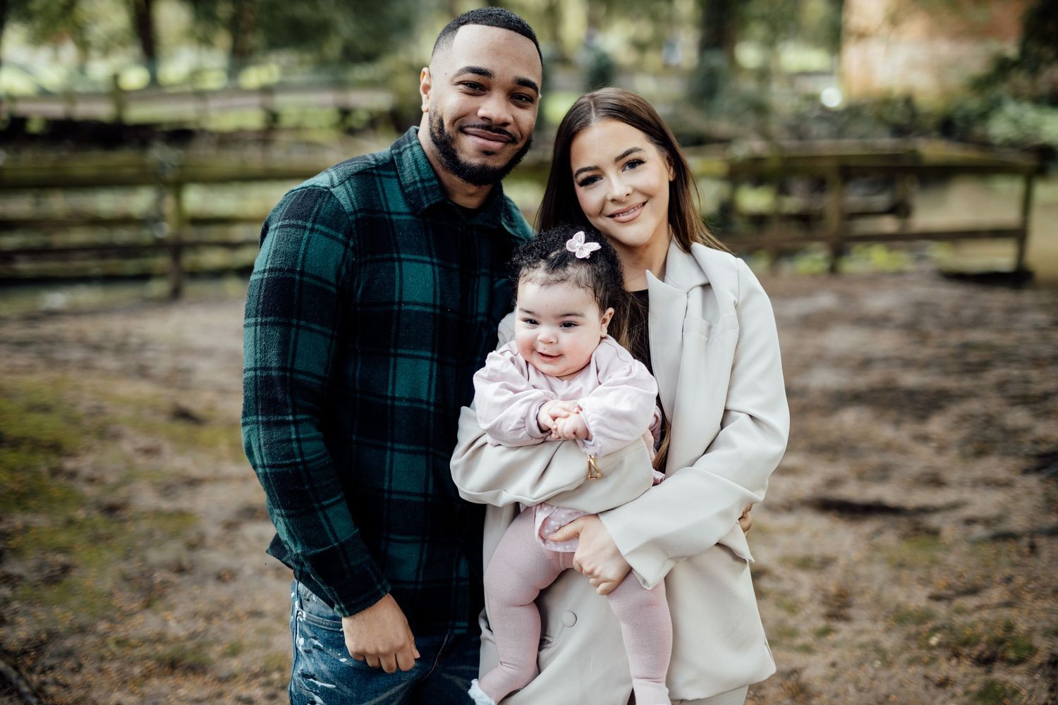 A family enjoys a tender moment together outdoors in winter clothing against a rustic wooden fence background.