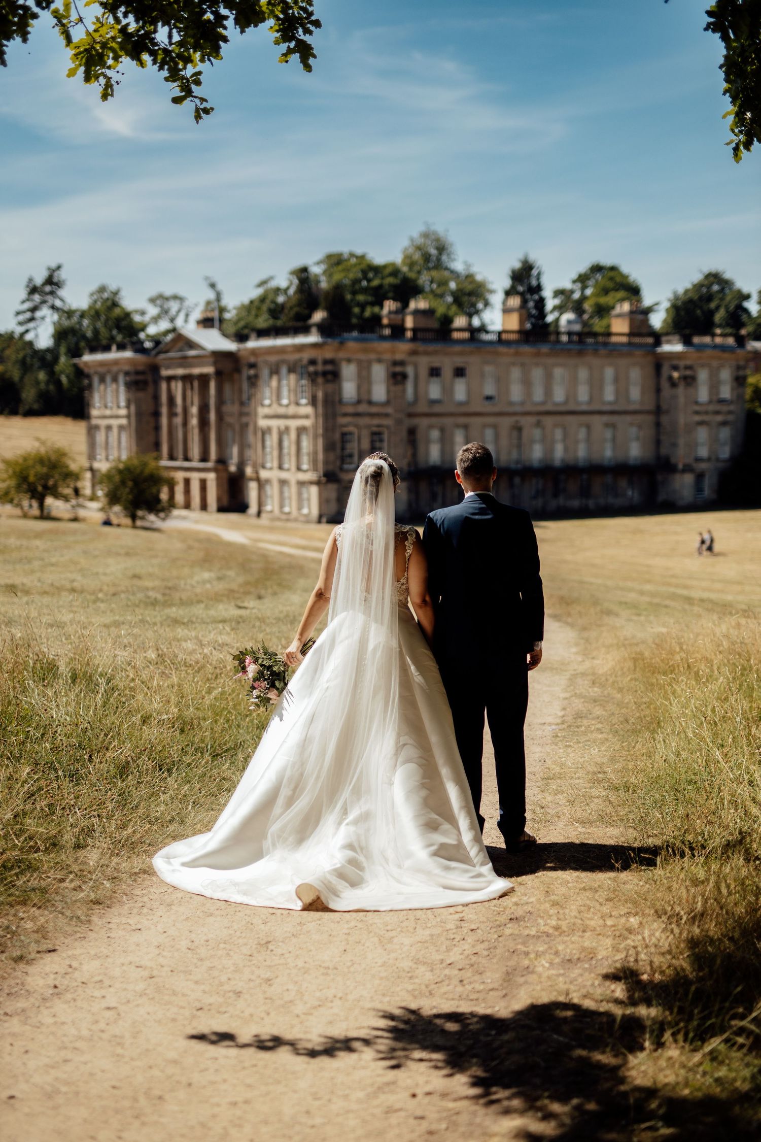 Wedding couple photographed from behind against historic mansion and sprawling grounds.