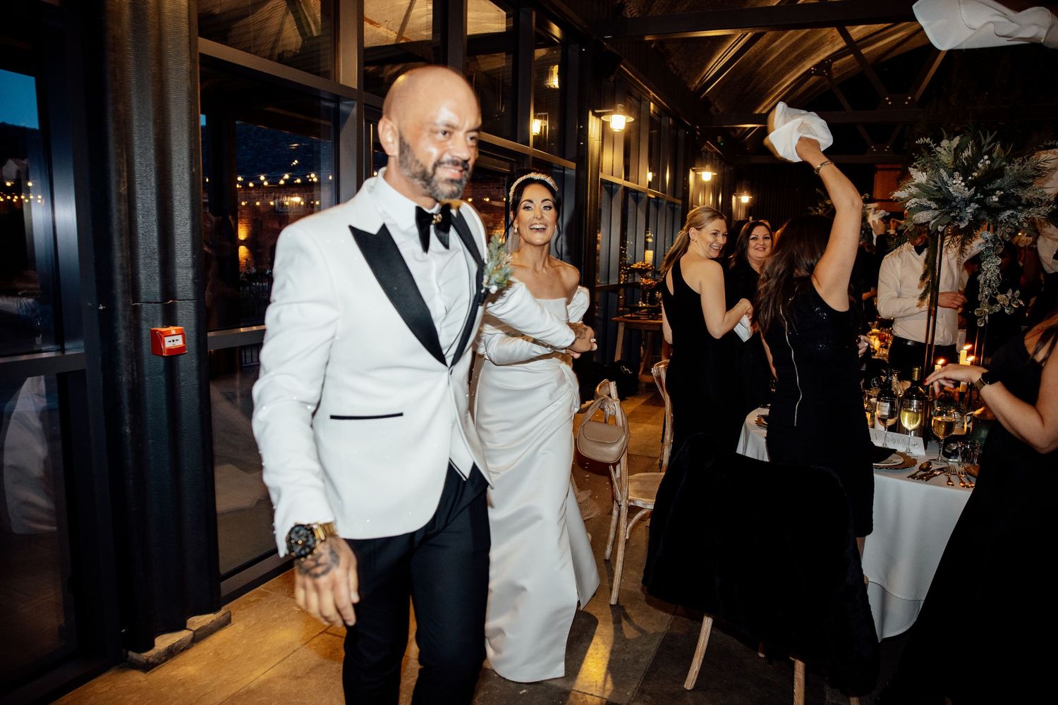 Wedding reception guests dance and celebrate in formal attire under warm lighting.