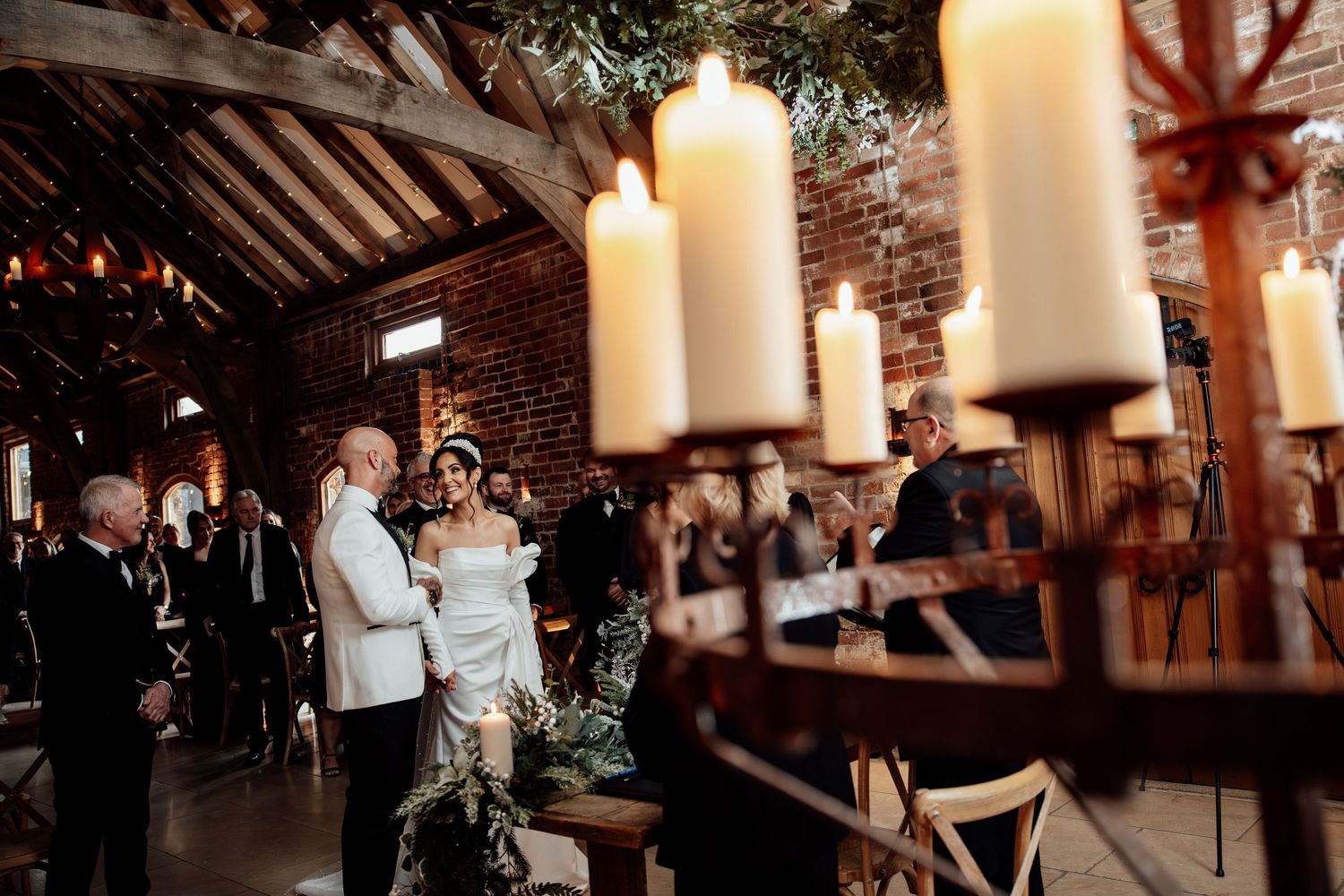 Wedding ceremony in a rustic venue with large white candles and exposed brick walls.