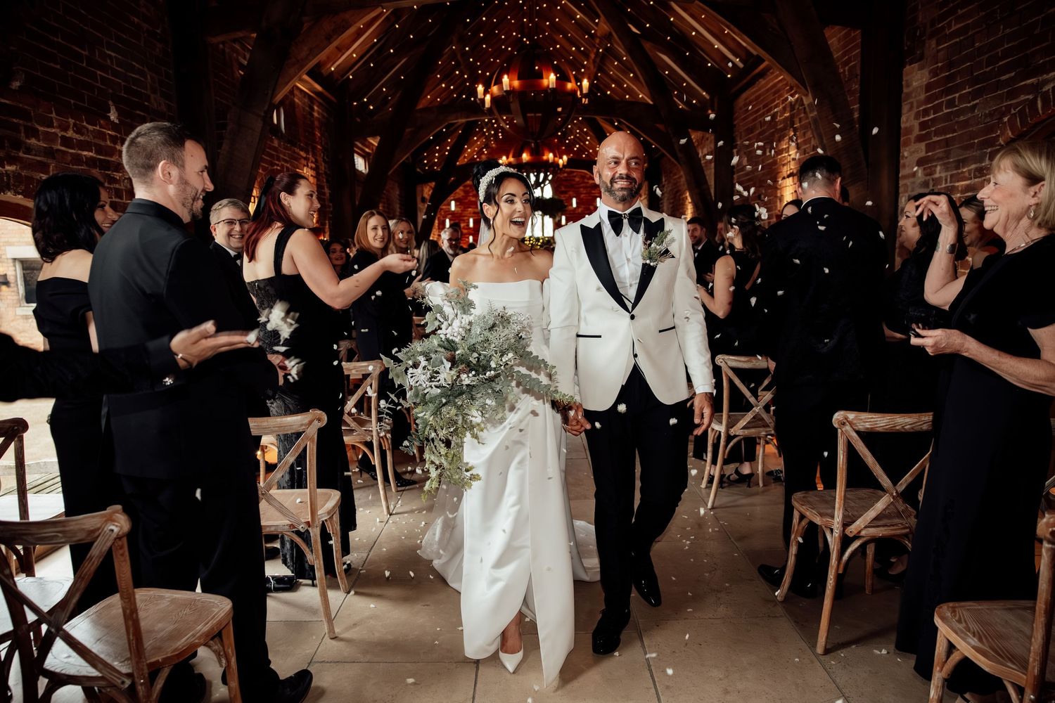 Wedding guests dancing and celebrating in a rustic brick-walled venue with warm lighting.