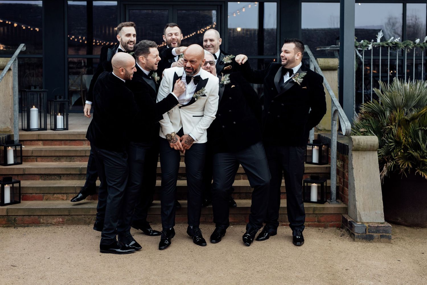 Groomsmen in black suits posing together at an outdoor venue.