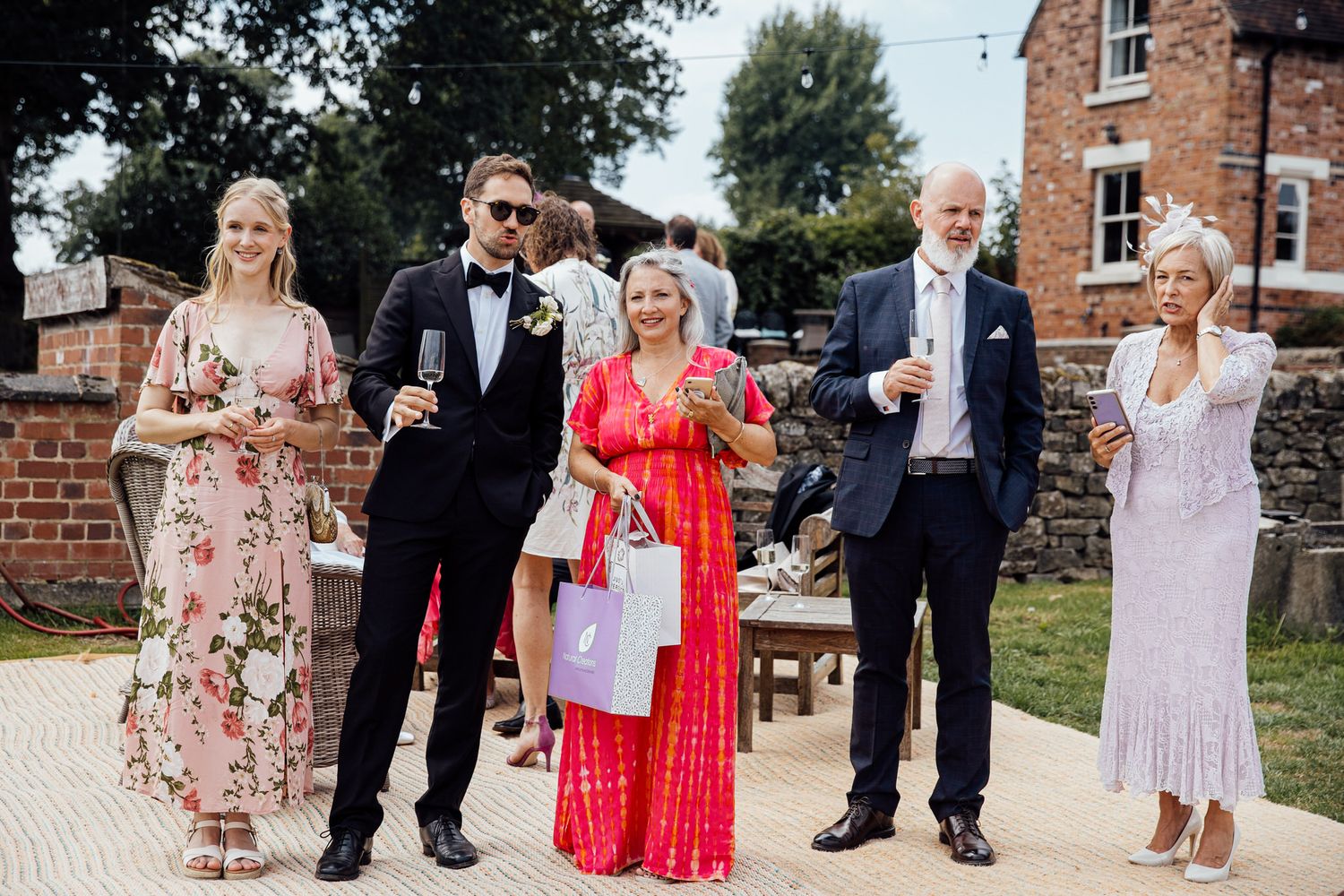 Wedding guests in formal attire raise their glasses during an outdoor celebration.