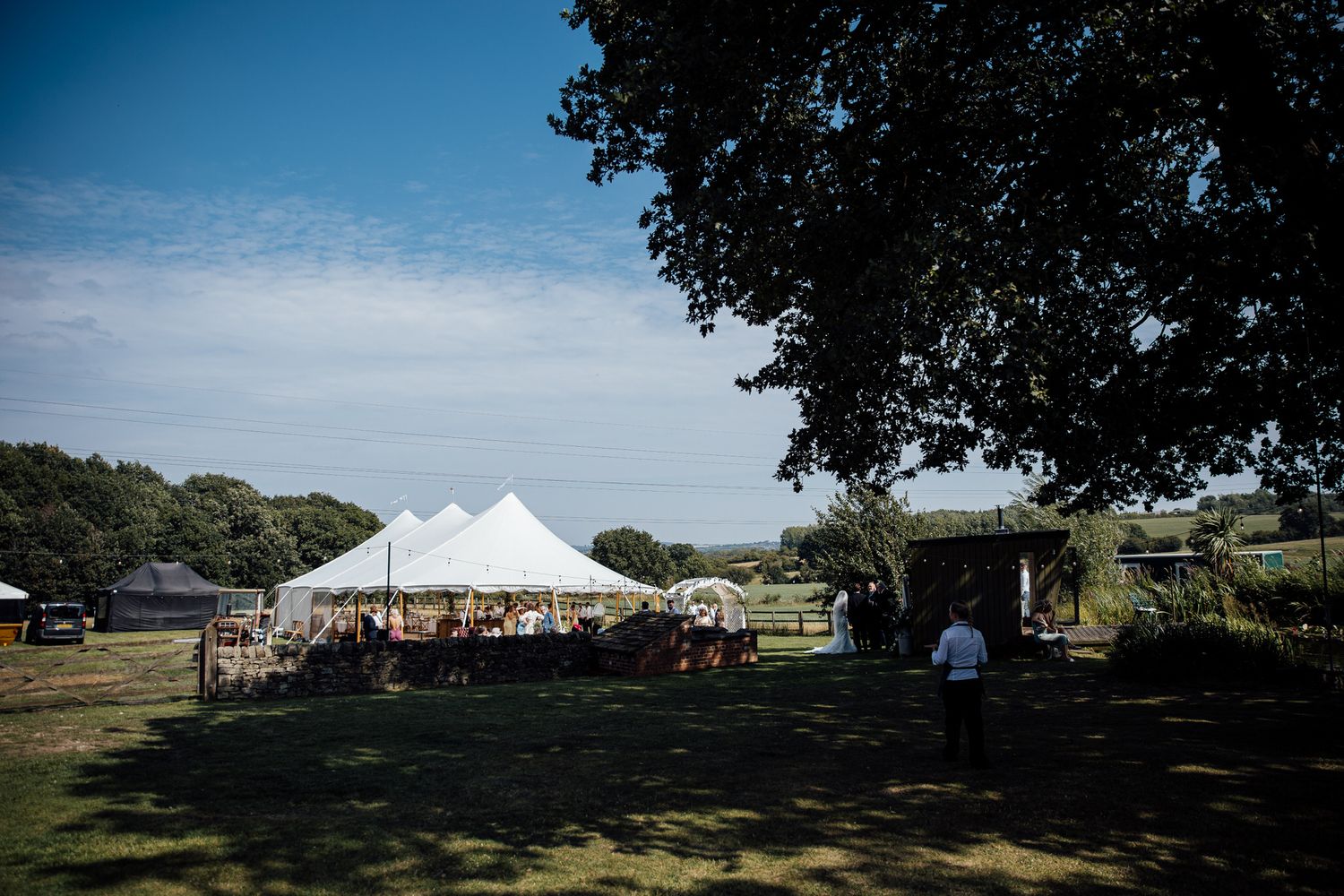 Panoramic view of outdoor wedding venue with white tent and trees under blue sky.