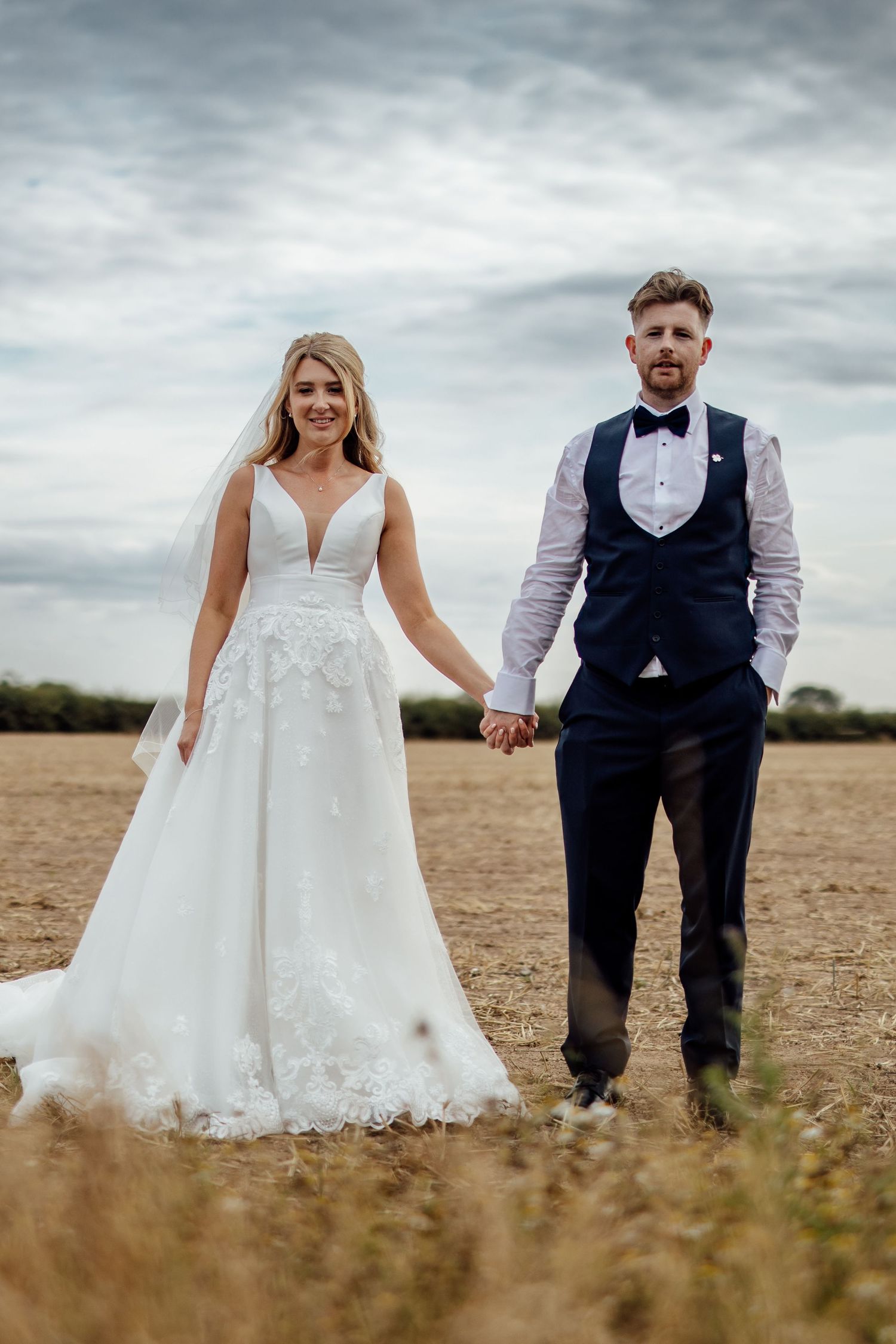 Artistic wedding photos taken in a wheat field under dramatic cloudy skies.