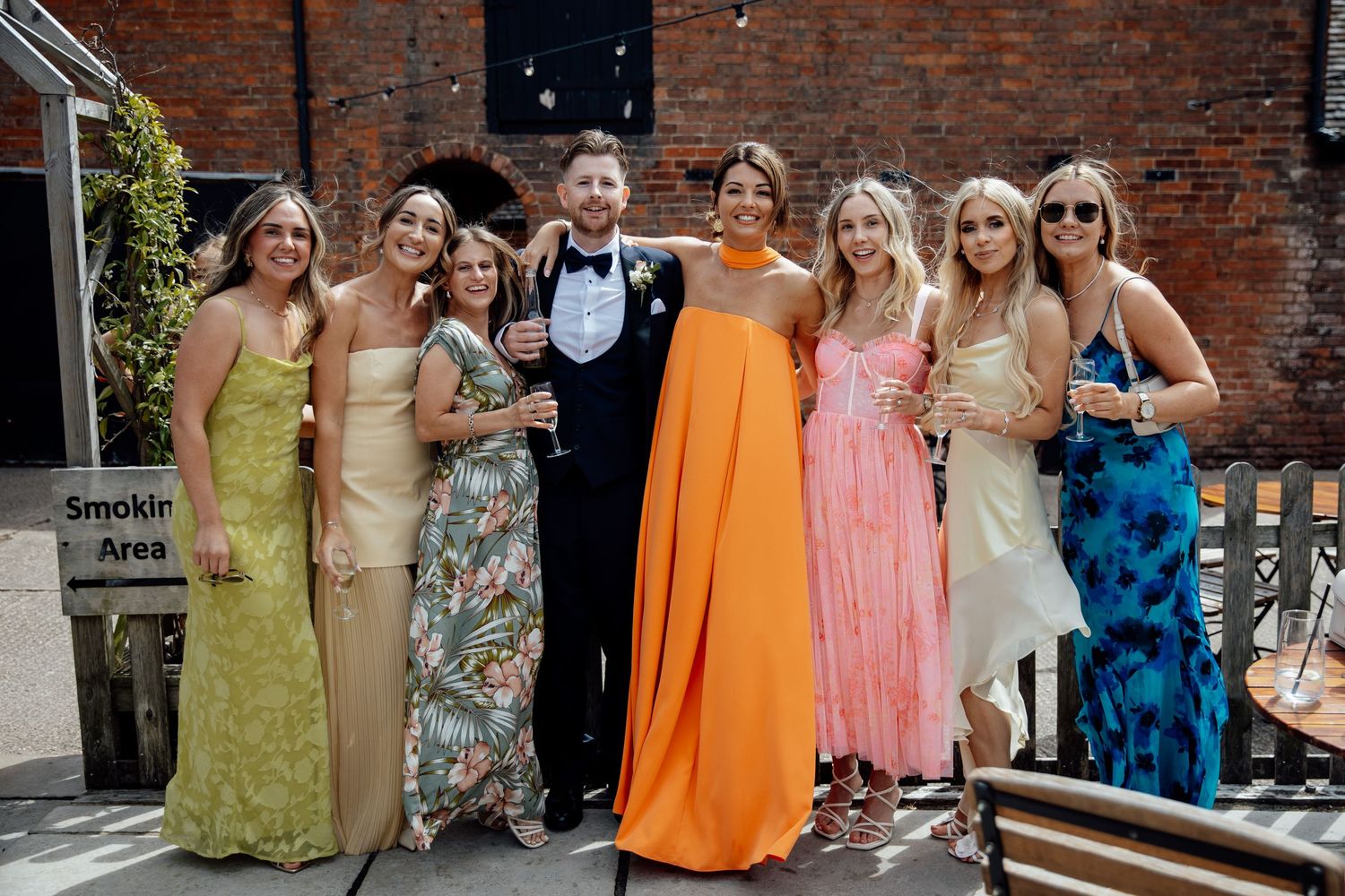 Wedding guests in colorful summer dresses gathered outside a brick building.