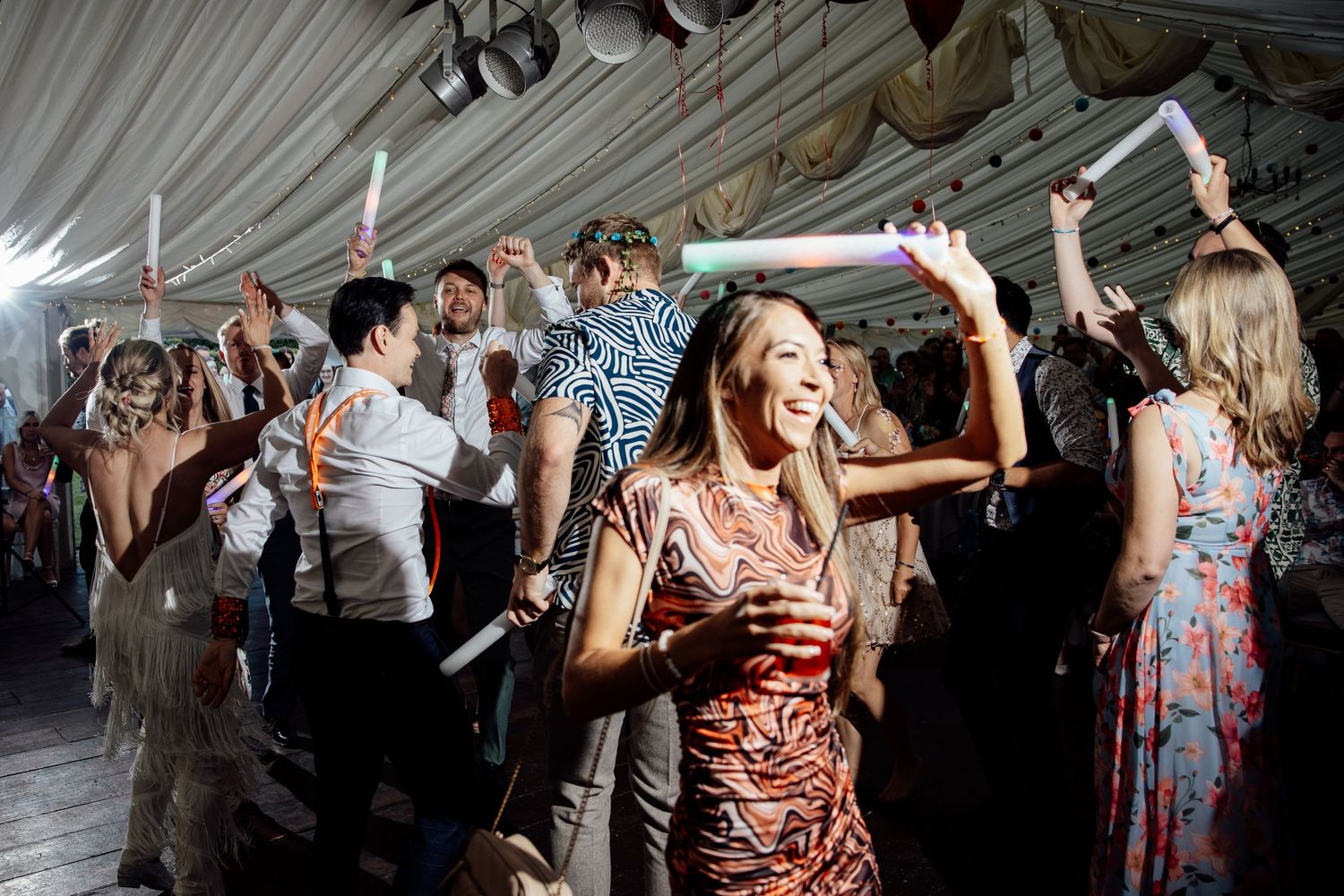 Energetic wedding reception with guests dancing under white tent lighting.